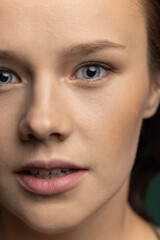 Fototapeta premium Close-up young beautiful adorable girl's face isolated over dark green studio background. Natural beauty, wellness, well-kept skin, herbal cosmetics concept