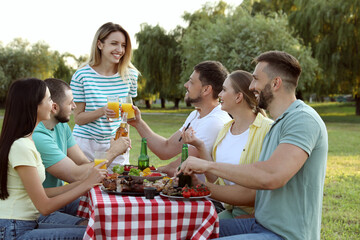 Happy friends with drinks and food at barbecue party in park