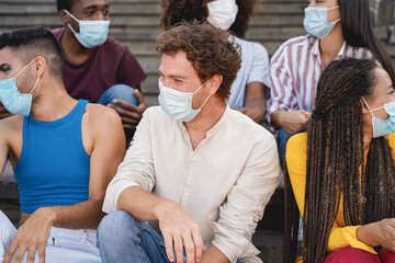 Young diverse people laughing together wearing safety mask outdoor in the city - Focus on center man face