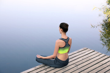 Woman meditating on wooden pier near river