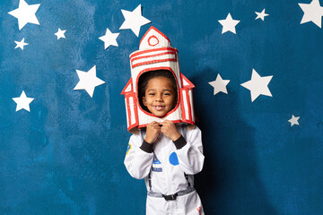 Rocket afro-american little boy in space suit playing astronaut on blue background with white...