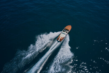 Top view of a wooden powerful motor boat. Classic Italian wooden boat fast moving aerial view. Luxurious wooden boat fast movement on dark water. - obrazy, fototapety, plakaty