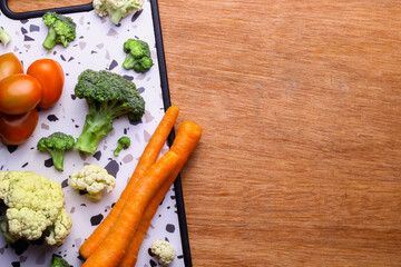 Top view. Assorted vegetables. Tomatoes, carrots, broccoli, and a cutting board on a wooden table with space for text.