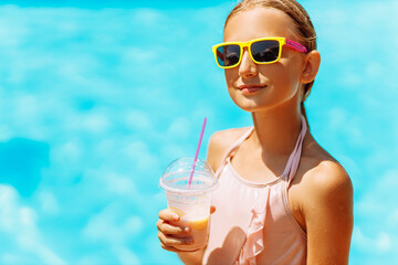 Little girl in sunglasses drinking a cocktail on vacation near the pool while on vacation in a warm tropical country, on a sunny warm summer day