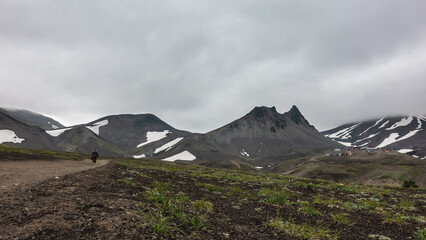 A dirt road runs through the valley to the mountains. A lonely man is walking along the path. A...