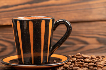 Roasted coffee beans scattered on a wooden surface and a coffee cup with a saucer close-up, selective focus.