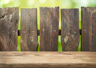 Old wooden table top with old fence on green defocused background