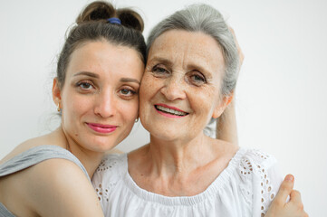 Happy senior mother is hugging her adult daughter, the women are laughing together, sincere family of different age generations having fun on white background