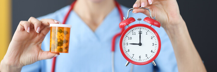 Smiling doctor holds red alarm clock and medication in his hand