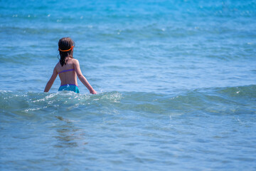 Concept: Drowning dangers for kids and outdoor water safety for parents. Beautiful young girl swims alone in the sea. Copy space. Horizontal image.