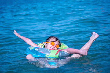 Beautiful young girl with inflatable ring swimming in exotic sea. She is engaged in water gymnastics. Humorous image. Copy space for text or design.