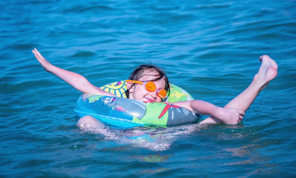 Beautiful young girl with inflatable ring swimming in exotic sea. She is engaged in water gymnastics. Humorous image.