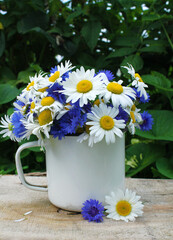 bouquet of chamomiles and cornflowers in a white mug with a handle on a wooden table. 