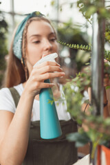 Young businesswoman sprays plants in flowerpots on rack