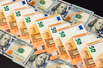 50 euros and 100 dollars lie in a row, banknotes of euro and dollars on a black background.
