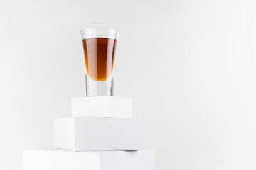 Golden whiskey in shot glass in sunlight with shadow on top of abstract white podiums, alcohol drink in single geometric minimal style.