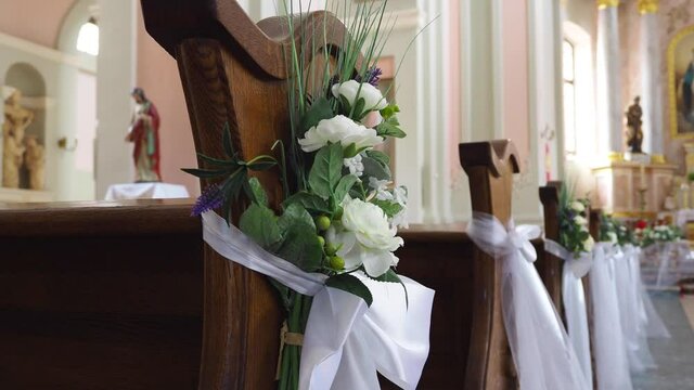 Wooden benches decorating by flowers and white bands for wedding celebration at the katolic church. Flowers decoration for the weddin ceremony. Close-up of video 4k resolution.
