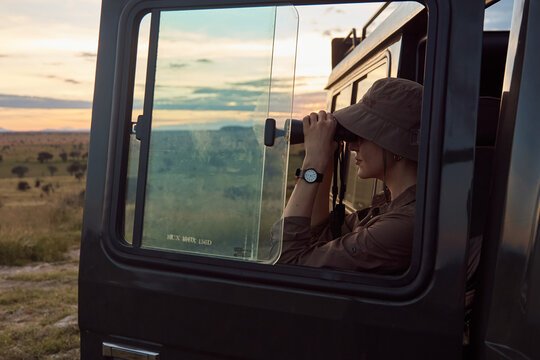girl standing around a tourist car and looking through binoculars. Against the background of the sunset