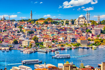 Fototapeta premium Touristic sightseeing ships in Golden Horn bay of Istanbul and mosque with Sultanahmet district against blue sky and clouds. Istanbul, Turkey during sunny summer day.