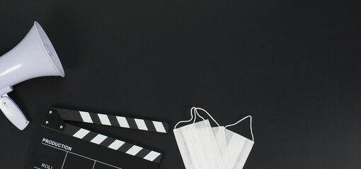 Black clapperboard with face mask and megaphone on black background.