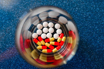 Water in a clear glass Cup and a dose of tablets in another glass on a blue surface
