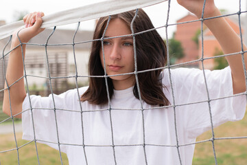 Sad teenage girl stands at the volleyball net. Troubled teenager on the school sports team.