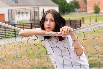 Sad teenage girl stands at the volleyball net. Troubled teenager on the school sports team.
