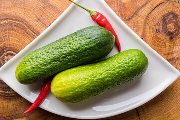 Two fresh green cucumbers with chili peppers on a white saucer.