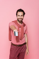Smiling man holding blurred credit card isolated on pink