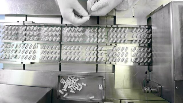 Factory employee is replacing some of the pills on the conveyor