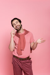 Positive man looking up while talking on smartphone isolated on pink