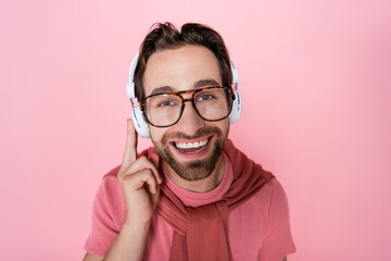 Smiling man in eyeglasses and headphones looking at camera isolated on pink