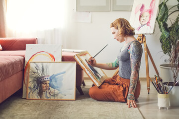 Cute red-haired girl hipster woman with tattoos draws on easel, creativity and self-expression,...
