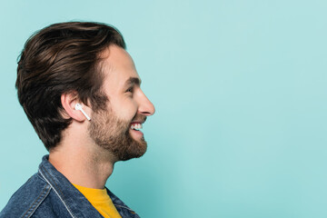 Obraz premium Side view of young man listening music in earphone isolated on blue