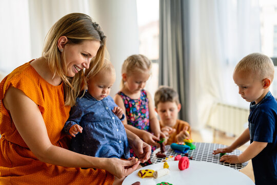 Mother or nursery teacher teaches her children to work with colorful play clay toys