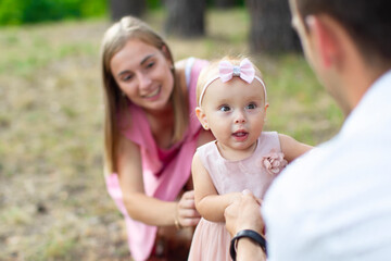 Fototapeta premium Husband, wife and their little daughter for a walk in the park. Happy dad and mom with one year old baby girl. Young family.