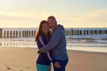 Happy romantic middle-aged couple enjoying a loving cuddle on a deserted tropical beach at sunset...