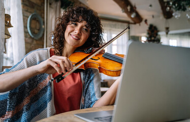 Woman student learns to play the violin online using a laptop.