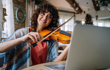 Woman student learns to play the violin online using a laptop. © NDABCREATIVITY