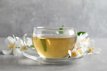 Glass cup of jasmine tea and fresh flowers on grey table