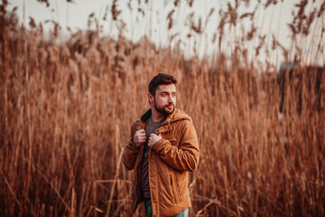 A man in a red jacket stands against the background of reeds