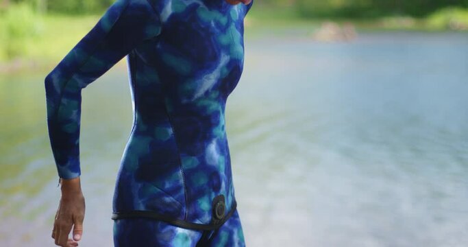 Young woman puts on blue wetsuit on the lake