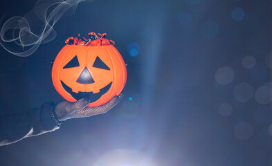 Fototapeta premium A bucket of candy in the form of a pumpkin lantern Jack on a black background in a hand. Halloween banner place for text.