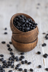 Fototapeta na wymiar Wooden bowls full of dry black beans on aged wooden table closeup