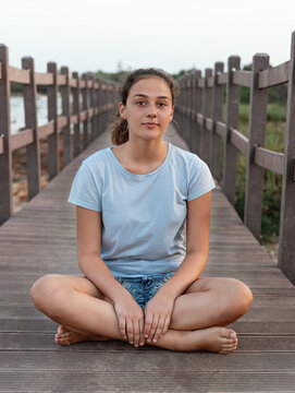 Teen Girl Sitting Cross Legged On The Walkway By The Sea