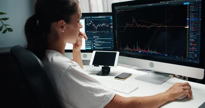 Female trader looks at the screen and analyzes the price movement on the stock market. Caucasian girl looks the cryptocurrency candlestick chart from home. Businesswoman works from home