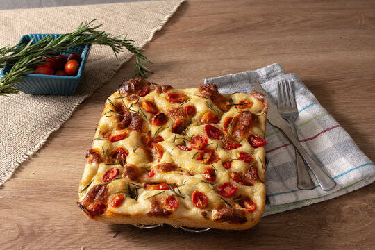 Homemade Italian Pugliese focaccia with rosemary and oil on rustic wood.