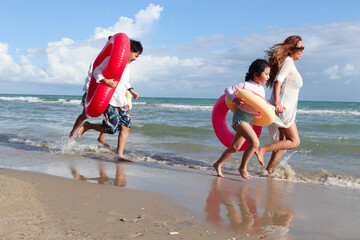 Children with parent wearing colorful inflatable swim ring running on summer beach, kids and adult on tropical sand beach, happy family spending time and having fun together on summer vacation.