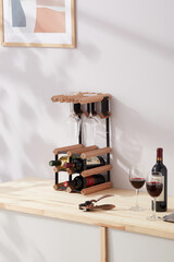 Interior photo: stylish wine rack with bottles is located on the table near wine glasses. Wine shelf with glass holders is made of wood and metal and designed to 6 bottles. 