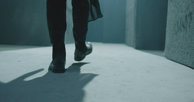 Close up of male legs in black boots.  Rear back view of man walking inside dark maze. Man walking inside dark room, corridor. Footage of mystical video. Shot on ARRI ALEXA Cinema Camera in slow motio